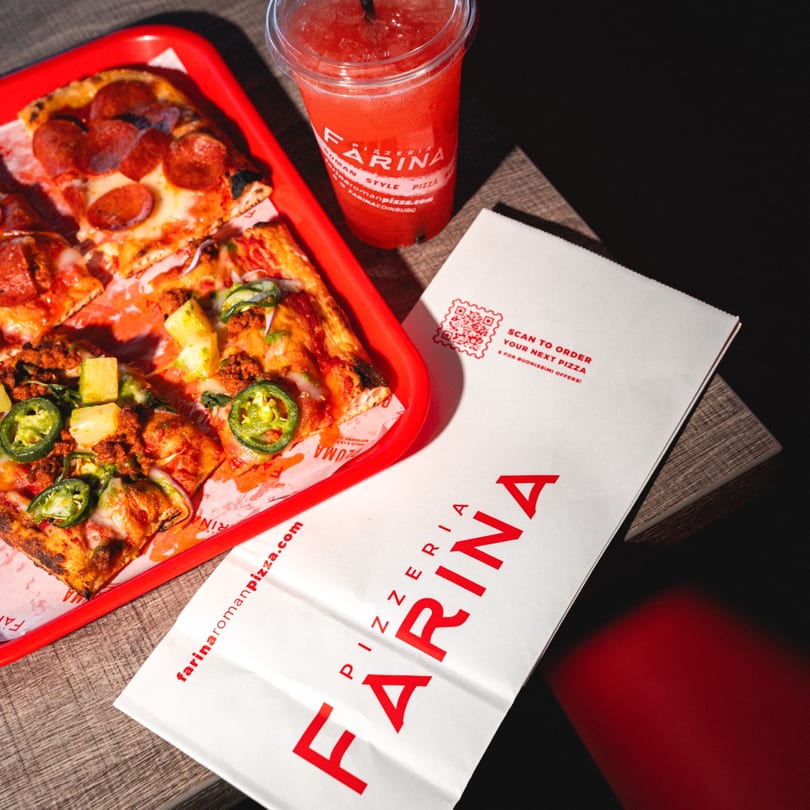 Farina Pizzeria Roman Style Pizza slices, a red drink, and a branded paper bag on a wooden table.