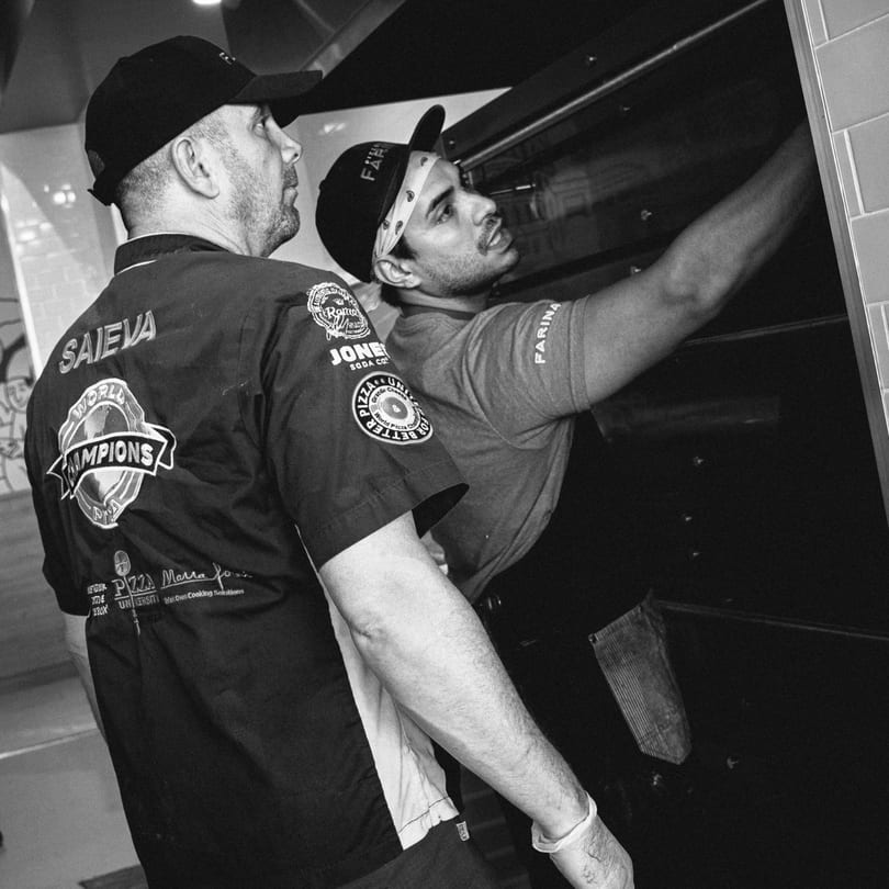 Two chefs, one wearing a "World Champions" shirt, looking into a large commercial oven.